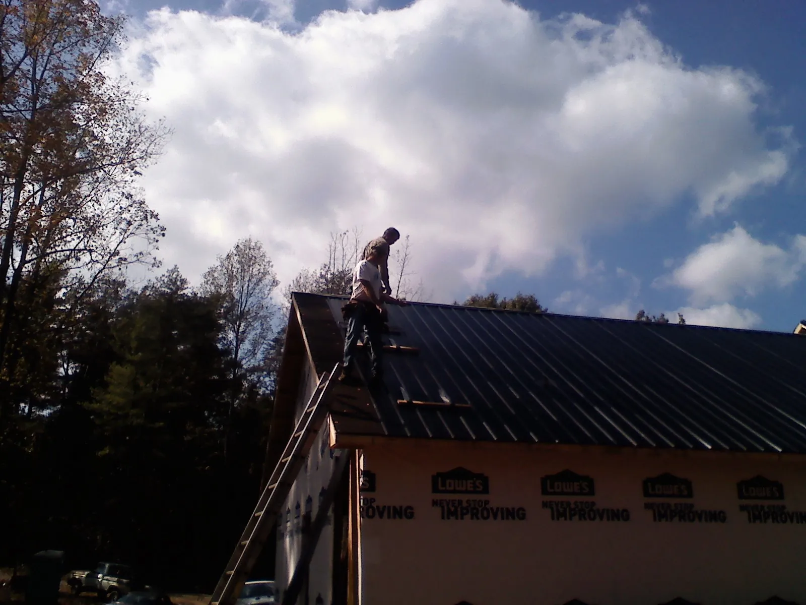 Roofer fastening dark metal panels high against a cloudy sky, from a Roof Inspection job in Powell